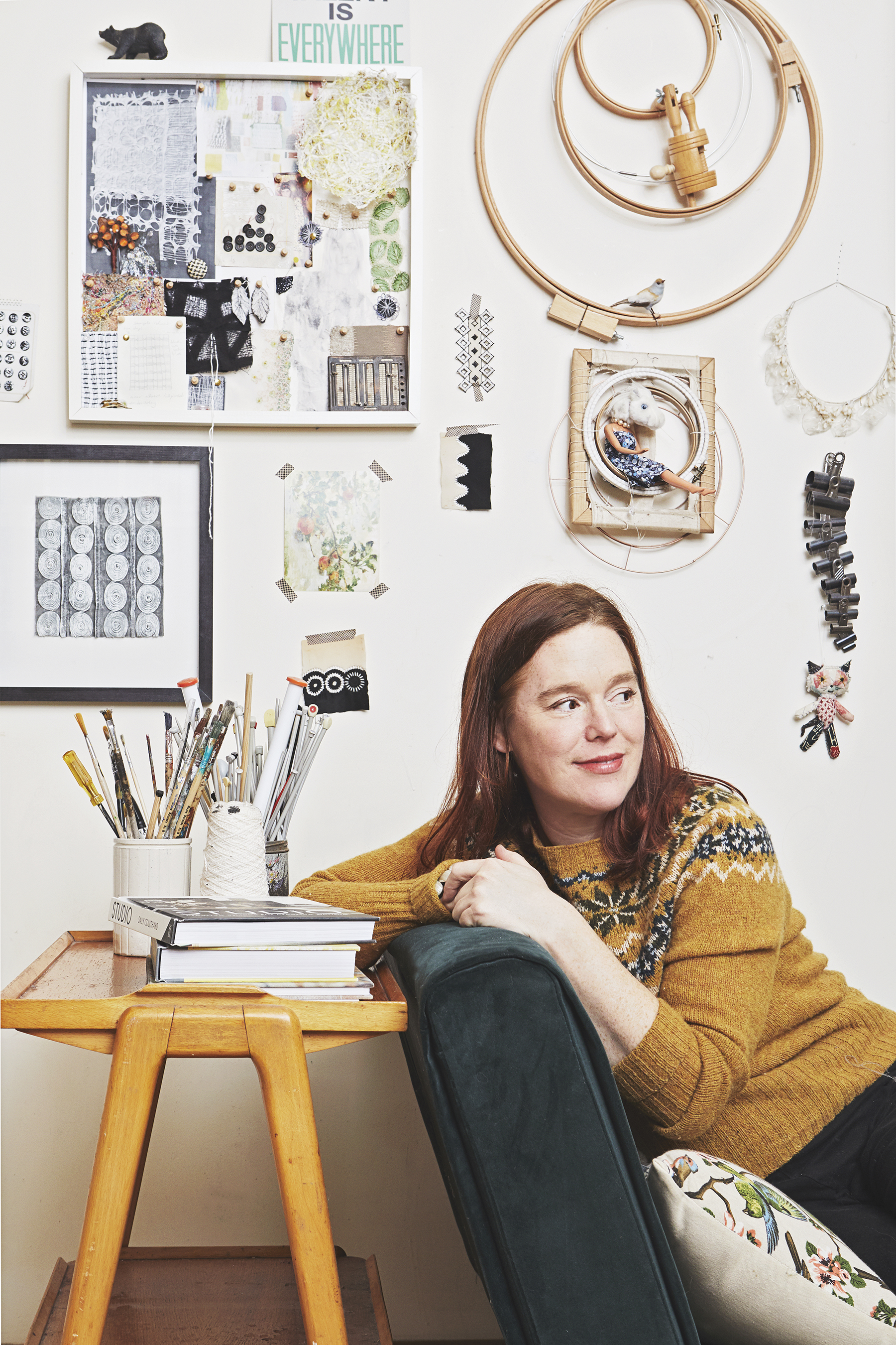 Textile artist Jayne emerson sits in her studio. Behind her is an inspiration wall full of textile samples and mood boards.